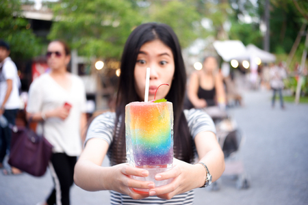 Young girl holding glass made of ice with smoothie, Blurry people.の写真素材