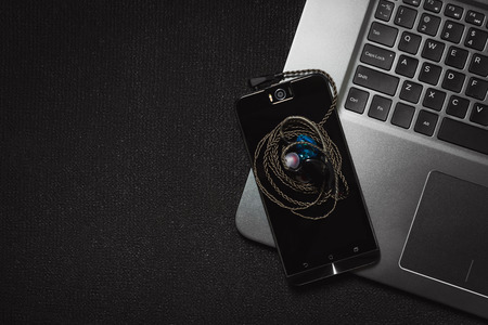 Top view smartphone with headphones and laptop keyboard on black background, Technology