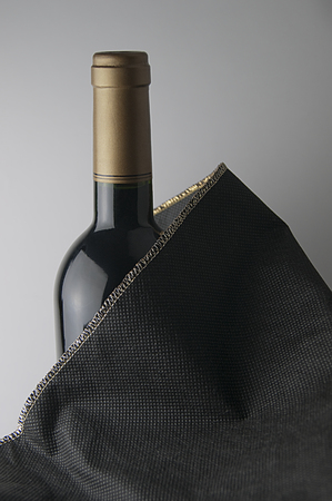 Bottle of red wine with golden cap. The bottle is covered with a black fabric with gold trimの写真素材