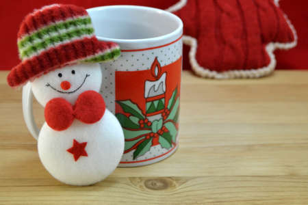 Mug with Christmas decor and santa claus toy on wood with red backgroundの写真素材