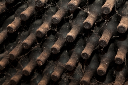 Old bottles of wine in rows in wine cellar. The webs of spiders and dust on the bottles betray their age.の写真素材