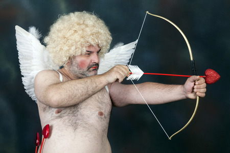Fat bearded mature hairy cupid with bow and heart arrow.の写真素材