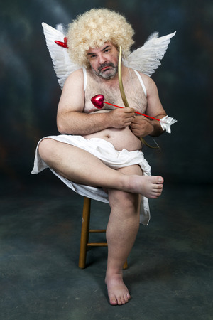 Fat bearded mature hairy cupid with bow and heart arrow.の写真素材