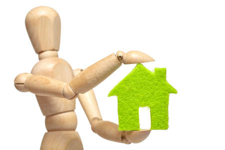 Wooden puppet holds small green house on white backgroundの写真素材