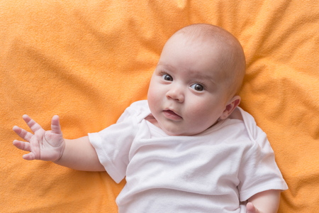 Portrait of a cute baby boy lying on orange blanket. Adorable seven month old happy child.の写真素材