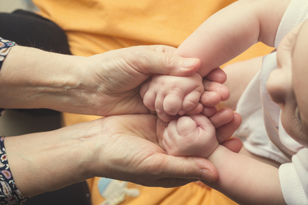 Hands of a young baby touching old hands of the elderly womanの写真素材