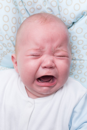 Portrait of a cute baby boy sitting and crying. Adorable seven month old child.の写真素材