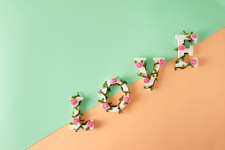 Creative layout with pink flower, leaves and Word LOVE in diagonal. Flat lay holiday background. Valentine's day minimal concept.の写真素材