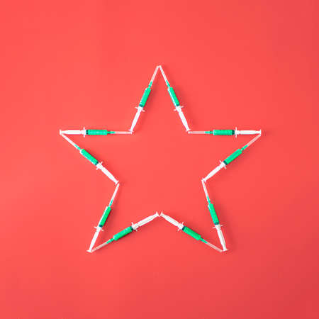Christmas star made of green vaccine on red background. Minimal New Year and christmas  concept. Winter holidays background.の写真素材