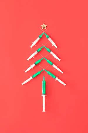 Christmas tree made of green vaccine on red background. Minimal Holiday composition. Creative Christmas wallpaper.の写真素材