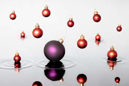 Colorful Christmas ball fall on the water like a rain. Red baubles touches the surface of the water...