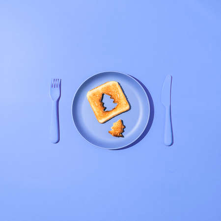 Toasted bread with a slice in the shape of a christmas tree on a blue plate. Minimal holiday flat...