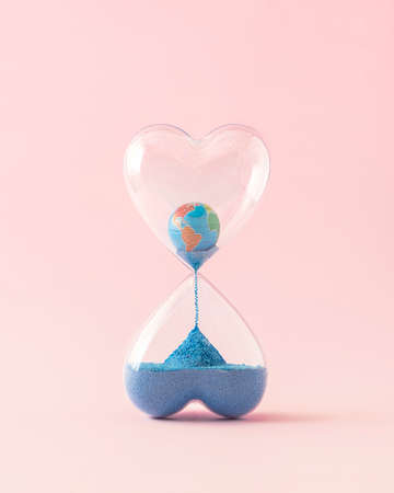 Creative layout made of hourglass with planet earth leaking like a blue sand. Running out of time concept. Minimal care composition.の写真素材