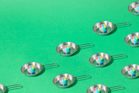 Pattern made of planet earth cooking in a metal pan on green background. Creative global warming...