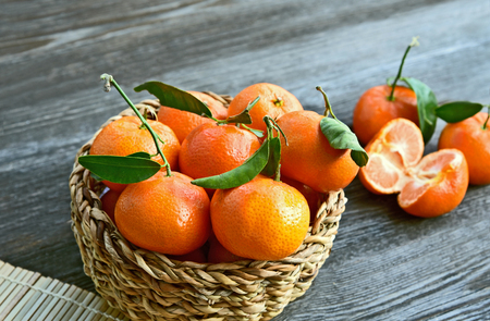 Fresh and Colorful of Mandarin orange and  green leafs with basket and wooden floorの写真素材