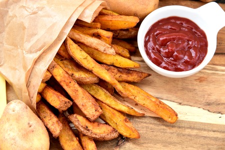 Homemade Crispy Seasoned French Fries.
French fries  with spicy seasoning in brown paper bag on wooden broad.の写真素材