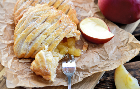 Easy Apple Turnovers (German name is Apfeltaschen) on brown paper with fresh red apples on wooden board and wooden floor.の写真素材