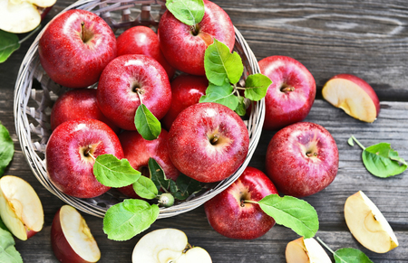 A lot of fresh Royal Red Gala apples with green leaf  in basket on wooden background.の写真素材