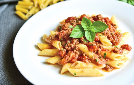 Penne  bolognese with basil leaf on white plate.の写真素材
