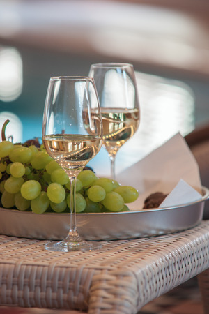 Wine in glasses near the grapes on a tray on the background of the poolの写真素材