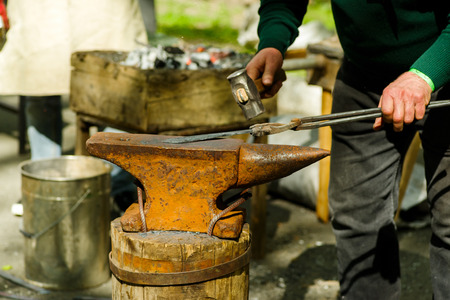 Blacksmith with a hammer and an anvil working on a product on the street