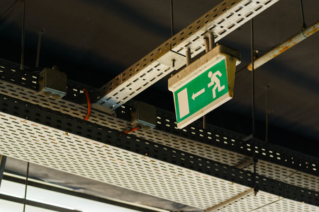the graphic sign of a running man to the exit hangs under the ceiling in an industrial roomの写真素材