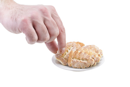 A man holds a biscuit cookie with sugar over a plate isolated on a white background