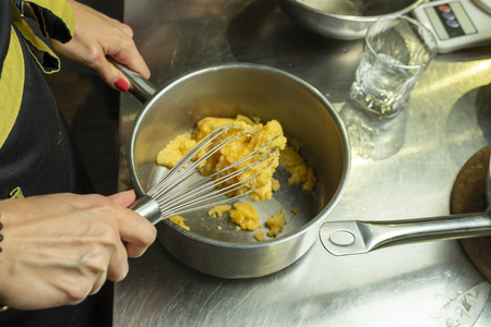 female hands prepare the cream by whipping in a metal plateの写真素材