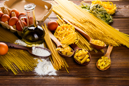 uncooked spaghetti and pasta on a table with eggs and flour and olive oilの写真素材