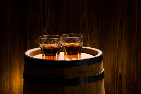 two glasses with strong alcoholic beverages  on a wooden barrel 