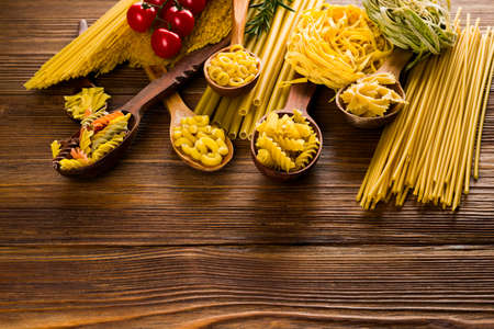 curly pasta in spoons on a dark table, different varieties of pasta.