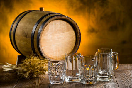 empty beer glasses on a wooden table with spikelets and a barrelの写真素材