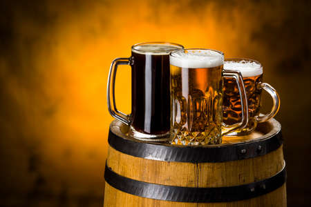 Dark and light and caramel beer with foam in the glasses for the company on a wooden table near the barrel,Dark Beer, Light Beer, Caramel Beerの写真素材