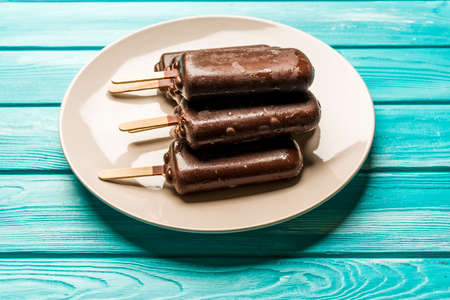 chocolate  ice cream with a stick on a plate, on a blue wooden table, top viewの写真素材