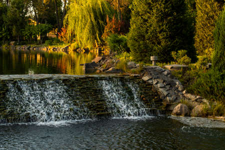 artificial pond with a waterfall in a landscape design in the sunsetの写真素材