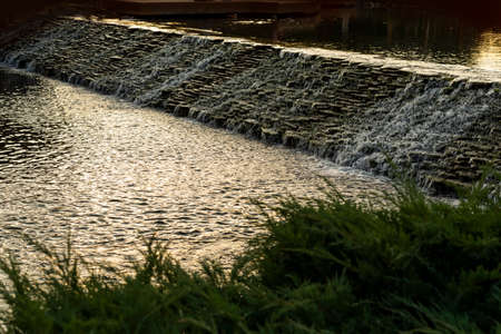 artificial pond with a waterfall in a landscape design in the sunsetの写真素材