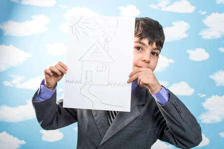 boy in jacket holding a pencil in his mouth and thinks holding a cookie sheet of paperの写真素材