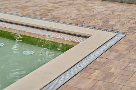 Walkway and ceramic tile with stone and metal gutter with grating around outdoor water pool outdoorsの写真素材
