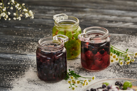 Preservation in jars with berries on a wooden table, a mix of blueberries, gooseberries, raspberries, black currantsの写真素材