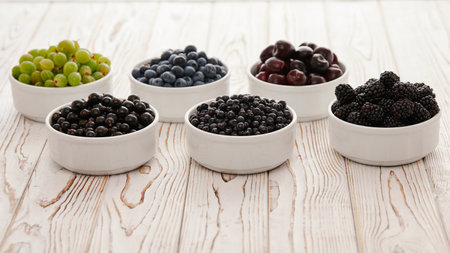 six bowls with seasonal berries, a mix of fresh berries on a wooden table, gooseberries, blueberries, currants, cherries, blueberries, blackberries,の写真素材