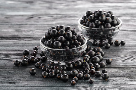 black currants in bowls on a wooden table, two servings of ripe berries in platesの写真素材
