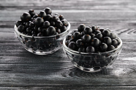 black currants in bowls on a wooden table, two servings of ripe berries in platesの写真素材