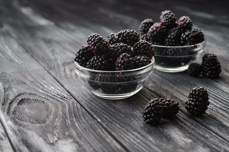 Ripe blackberries in glass saucers on a dark table background, close-up shotの写真素材