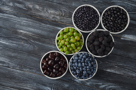 Ripe berries in bowls - blueberries, blackberries and black currants, sweet cherries, blueberries on a dark wooden background. dietary antioxidants and vitaminsの写真素材