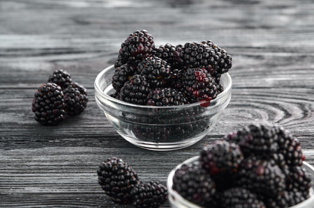 Ripe blackberries in bowls on a wooden table, close-up shotの写真素材