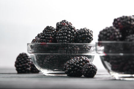 Blackberries in bowls on a light background on a wooden table, close-up shotの写真素材