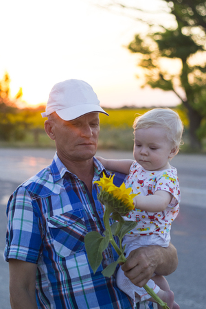 Grandfather with his grandson in his arms holding a sunflowerの写真素材