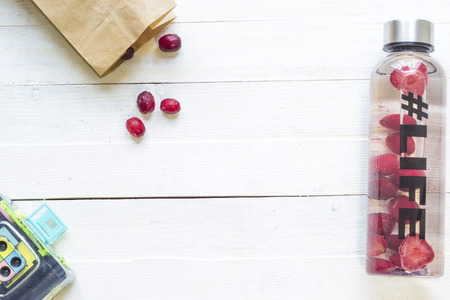 Bottle with refreshing drink, water with strawberry slices, with hashtag #life and package with frozen berries on white wooden backgroundの写真素材