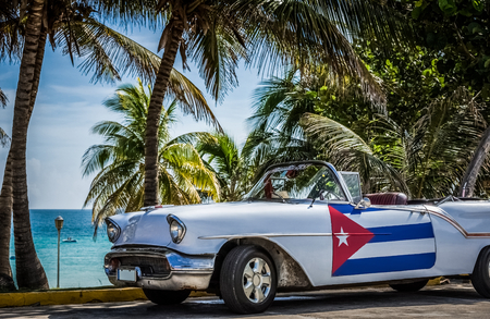 American white cabriolet vintage car with cuban flag on the side door parked under palms near the beach - Cuba Series Reportのeditorial素材