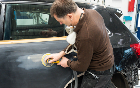 Car mechanic with dust mask grinds a car part in a service station - Serie car repair workshopの写真素材